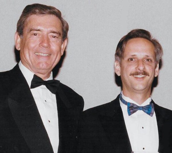Two mean in tuxedos and bow times pose for a photo.
