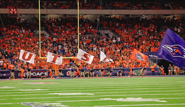Members of UTSA Cheer carry UTSA flags across the endzone