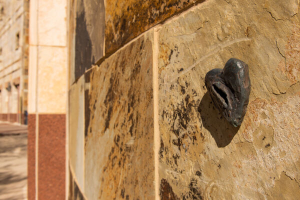 A closeup of a bronze heart, which is attached to an outdoor wall of a building.