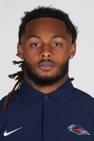 A man wears a blue polo with the Nike swosh and a roadrunner logo.