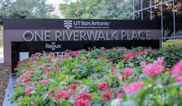 A sign reading "One Riverwalk Place" behind several pink flowers