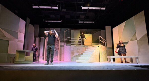 Four individuals in different placements on a stage as they look towards the audience.