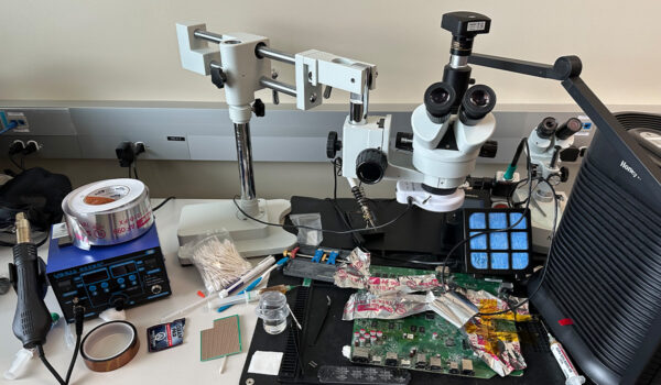 Lab setup with twin microscopes, circuit board, soldering equipment, and electronic tools.