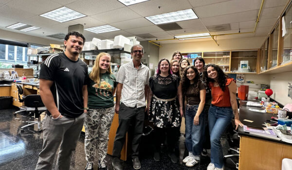 A group of 10 people stand beside each other in a lab.