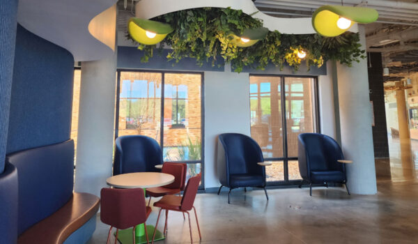 Modern lounge area with blue and red seating, round table, large windows, and overhead greenery.