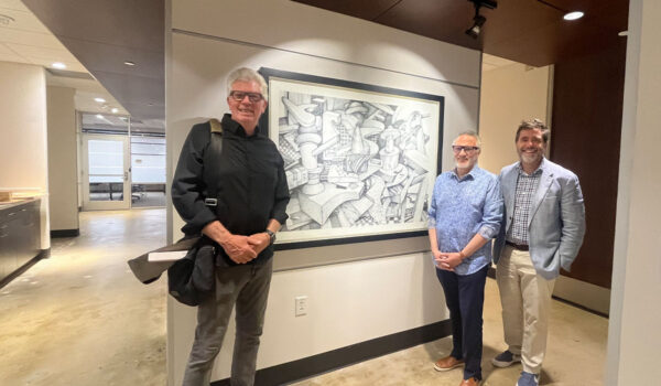 Three smiling men stand in a gallery hallway beside a large black-and-white abstract artwork.