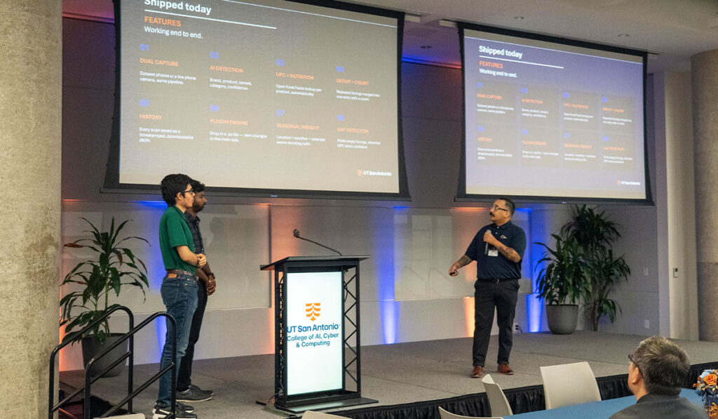 Three presenters speak beside a podium at a tech conference, with “Shipped Today” slides on screens behind them.