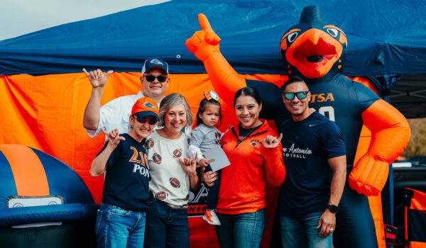 A family of UTSA football fans show the "Birds Up" hand sign next to an inflatable Rowdy the Roadrunner.