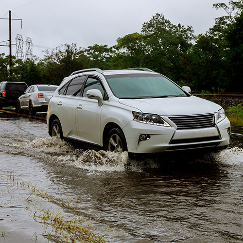 A white SUV drives down a flooded road.