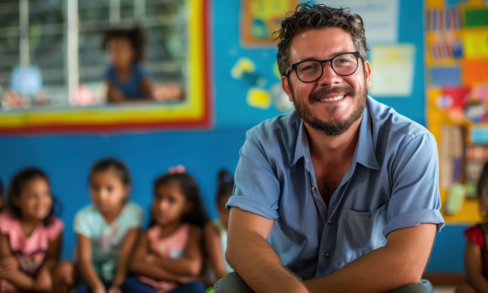 A middle aged teacher with glasses is in a classroom, children are seated in the background