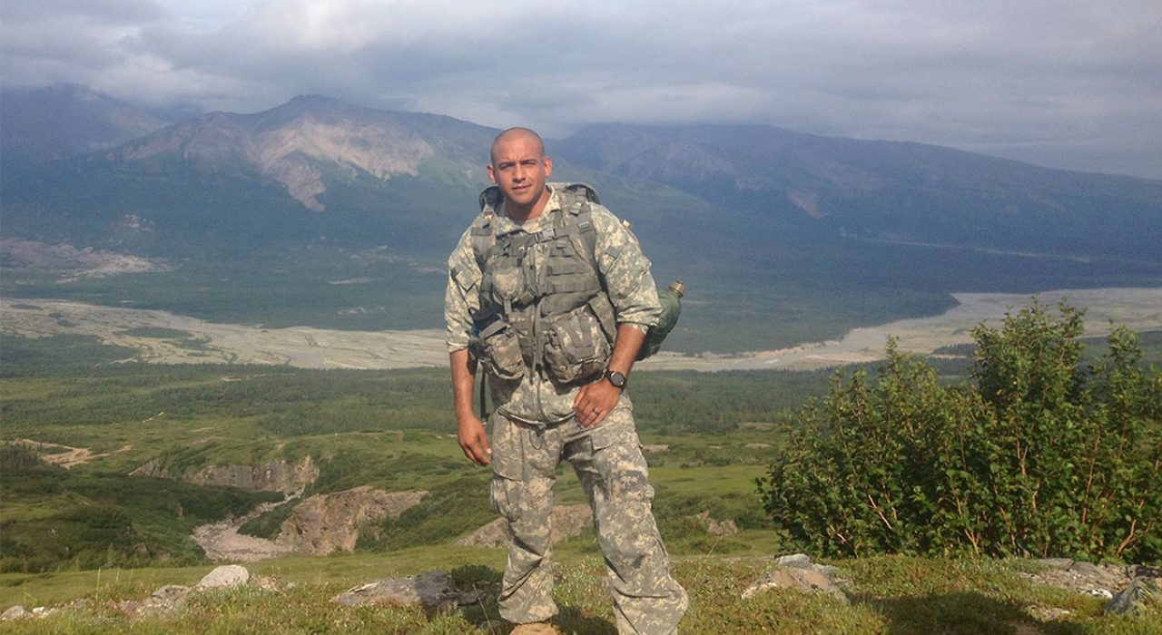 A combat medic poses for a photo in front of a mountain landscape