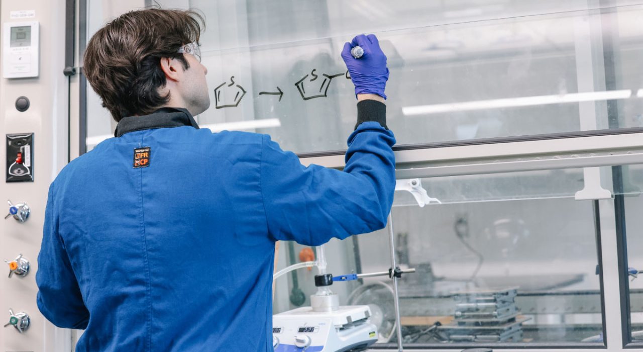 A chemist writes a formula on a glass lab hood with a dry-erase marker