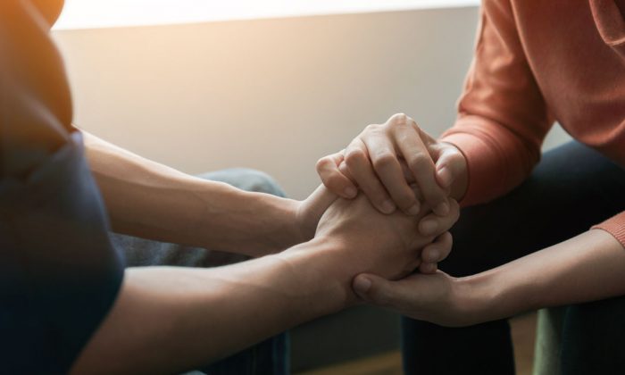 Two people grasp hands tightly near a window as light casts over their grip