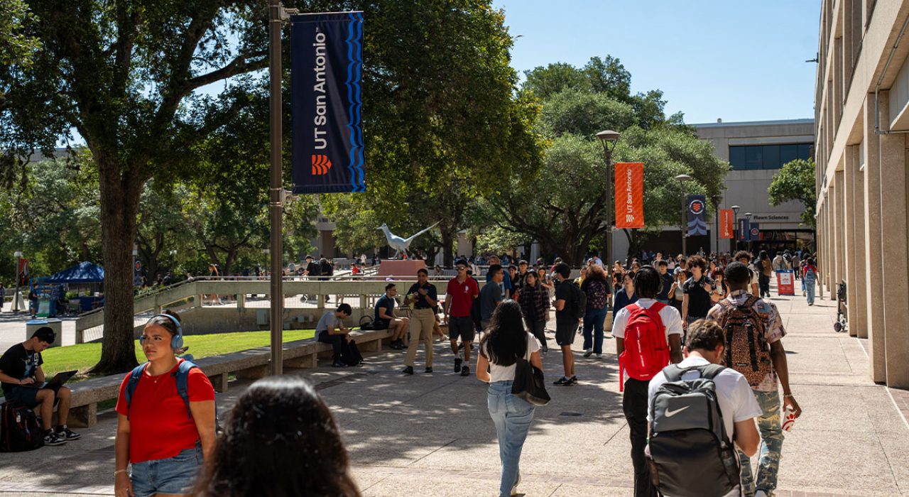 2025-main Groups of students are walking outside in an open space with orange banners in background.