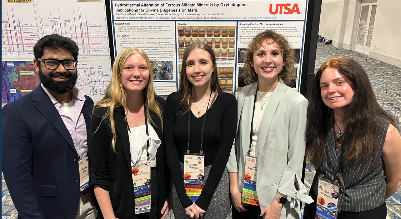 A man and four women stand in front of a large poster, which says "Hydrothermal Alteration of Ferrous Silicate Minterals by Oxyhalogens: Implications of Olivine Diagenesis on Mars."