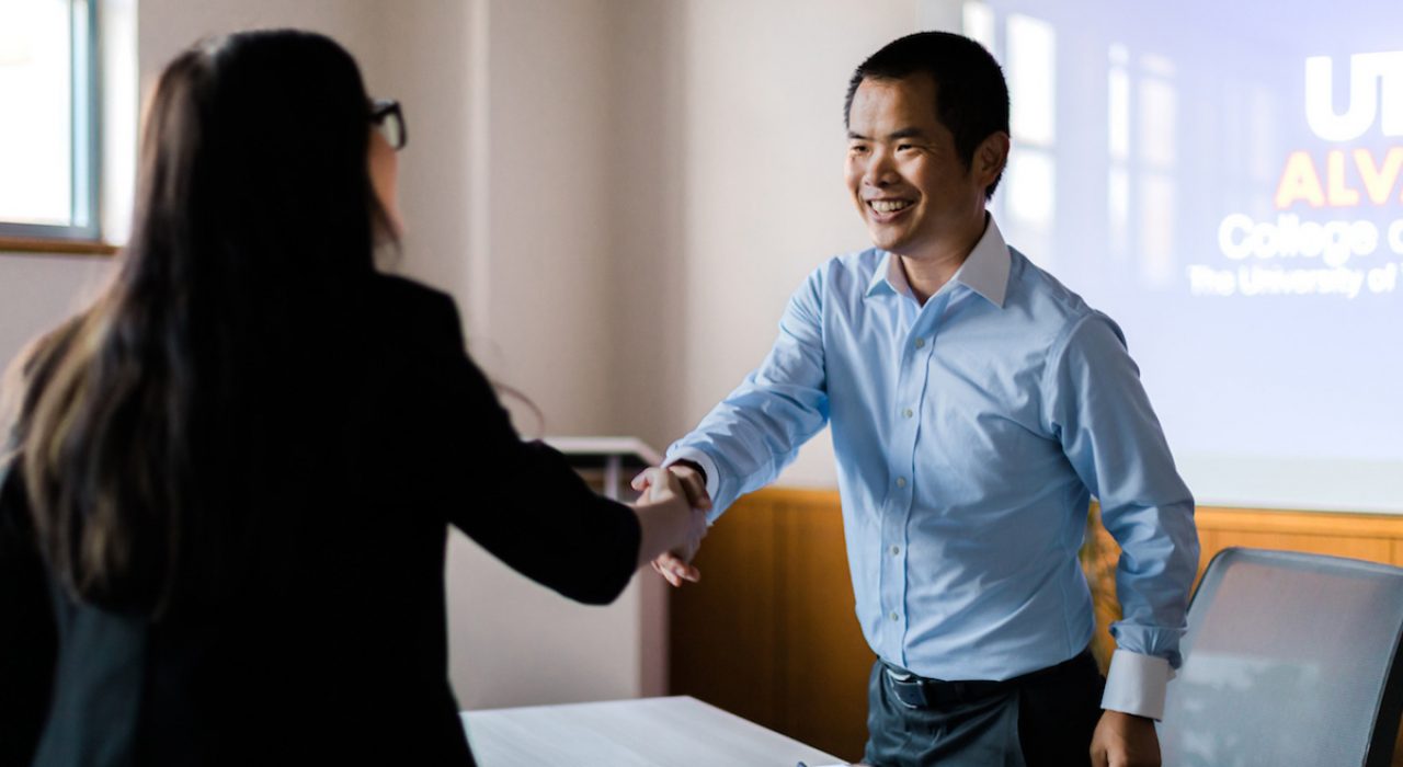 business advising a man and woman shake hands with college of business slide behind them