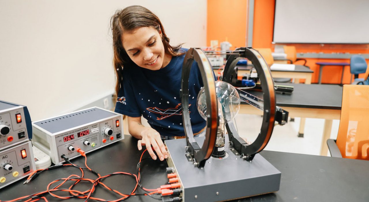 A woman sits in a lab as she works with some equioment, which has a large light bulb.