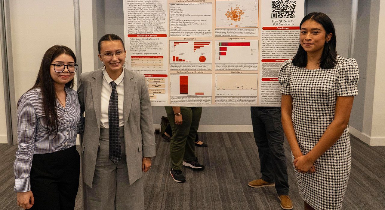 Three young woman smile as they side in front of a poster board of research.