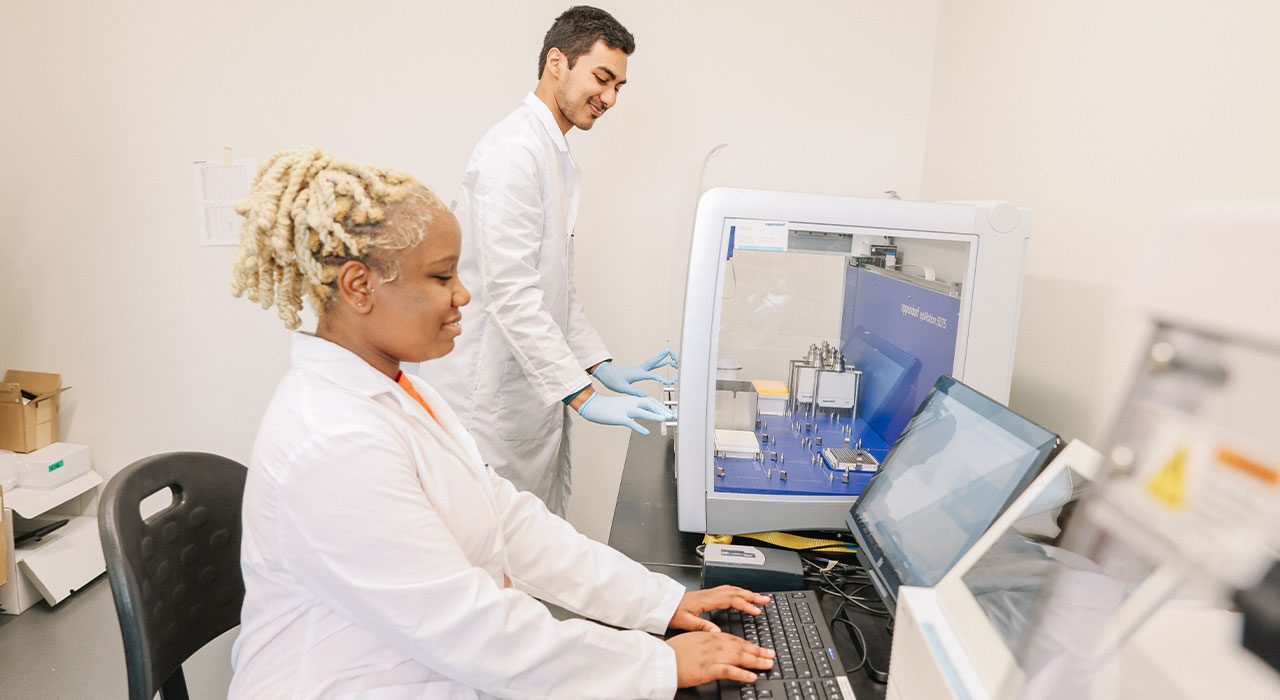 Two individuals in white coats work in a lab.