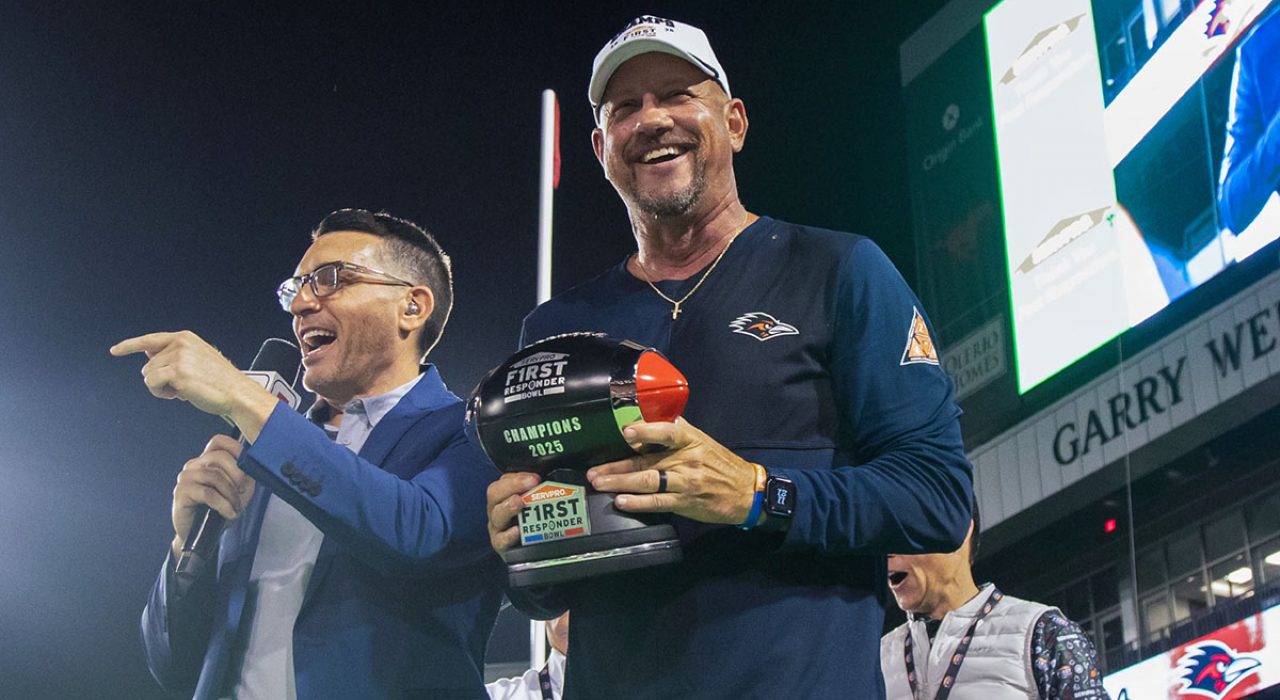 ESPN's Paul Carcaterra points while Jeff Traylor holds a trophy shaped like a football