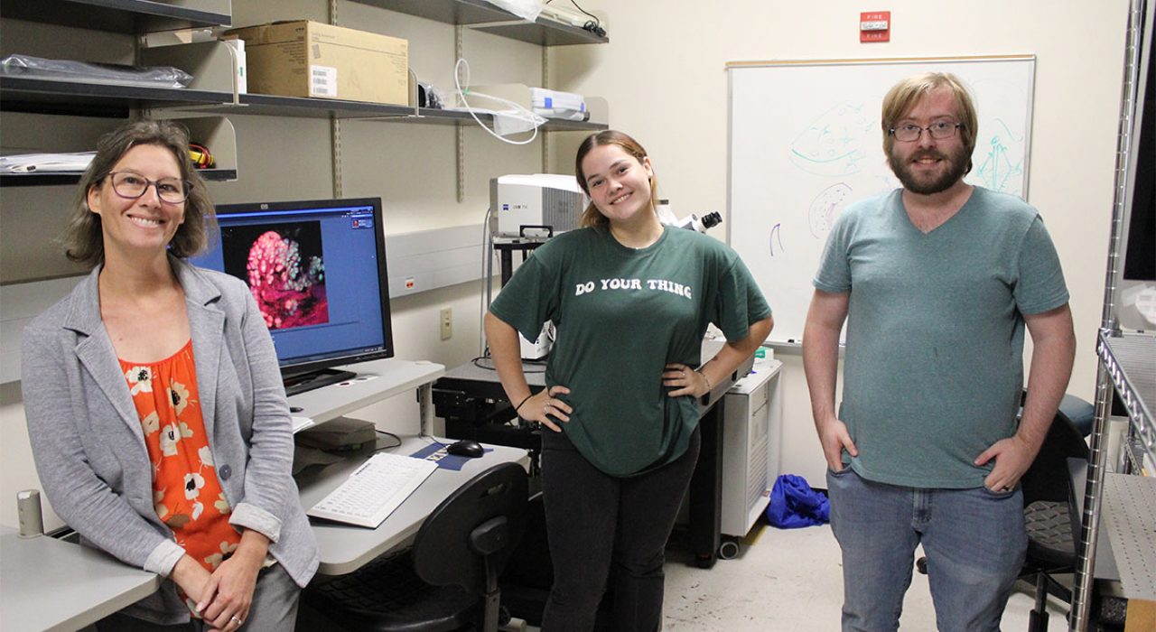 Three individuals smile as they stand in a lab.