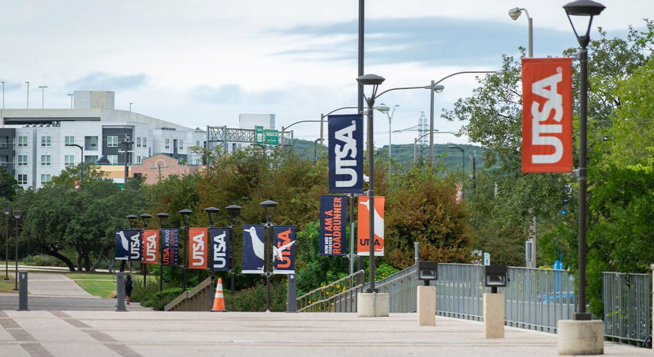 A walkway outdoors with light posts, which feature banners that read "U-T-S-A."