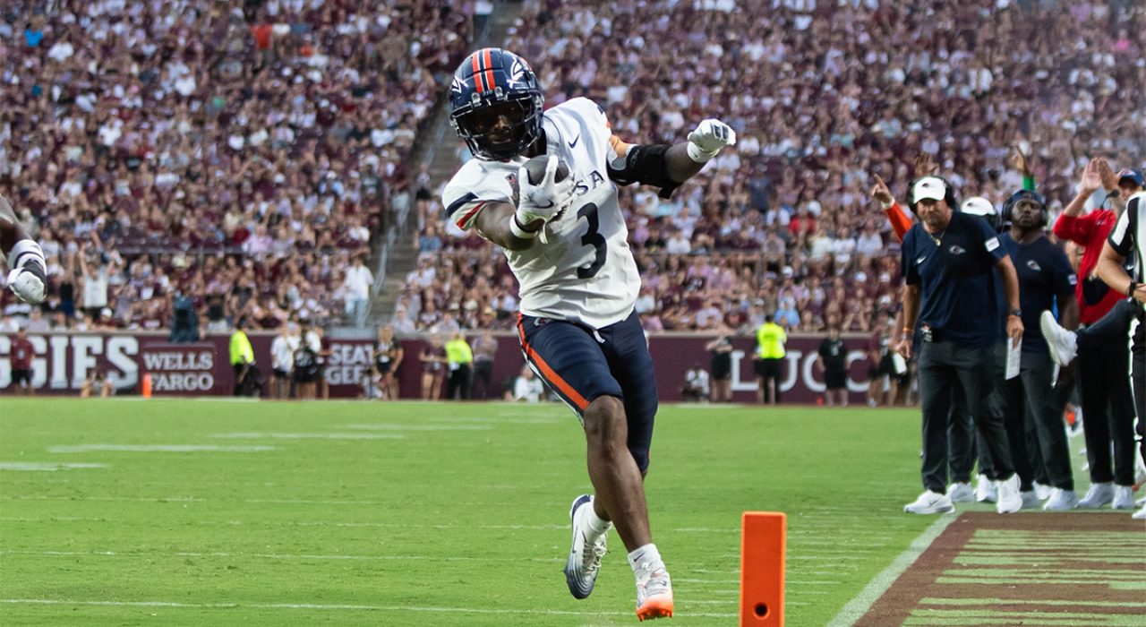 A man in full football gears down towards the sideline with a football.