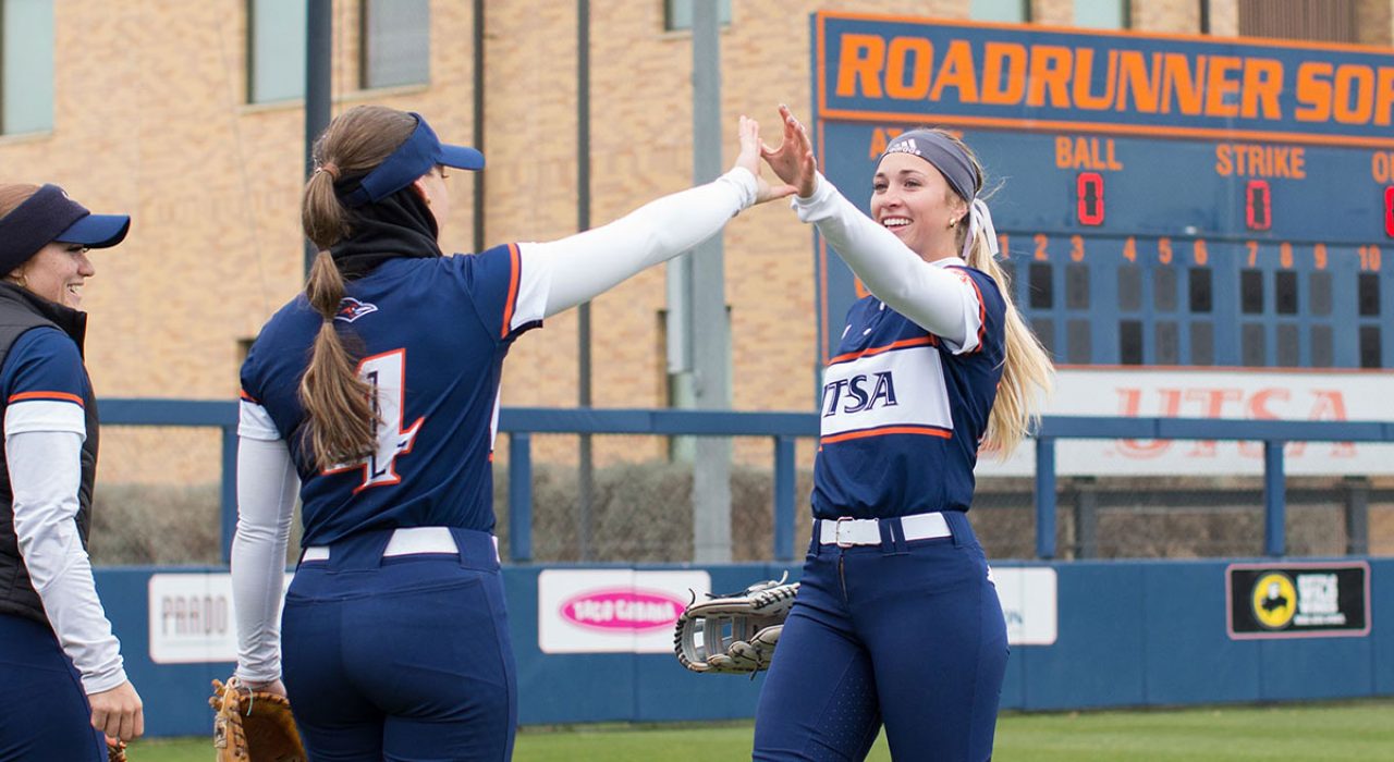 A young woman in a softball uniform high fives another person.