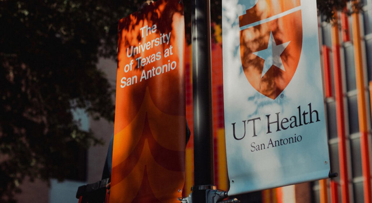 One orange banner that says, "The University of Texas at San Antonio." Another banner, which is white, says "UT Health San Antonio."